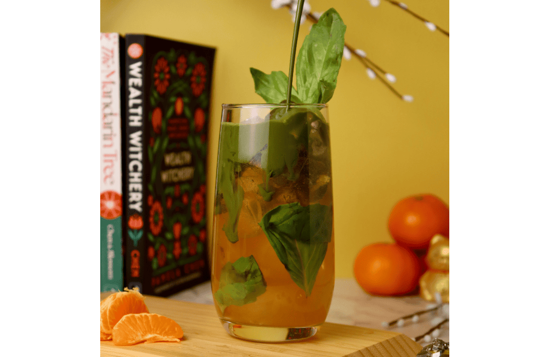 A matcha soda with orange mandarin juice on the bottom of the cup with green matcha pouring in from above.