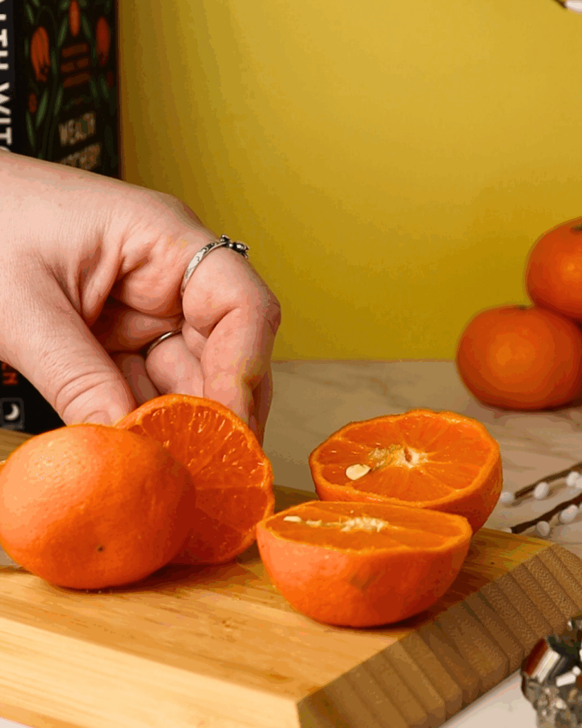 Fresh mandarin citrus being cut on a bamboo cutting board.