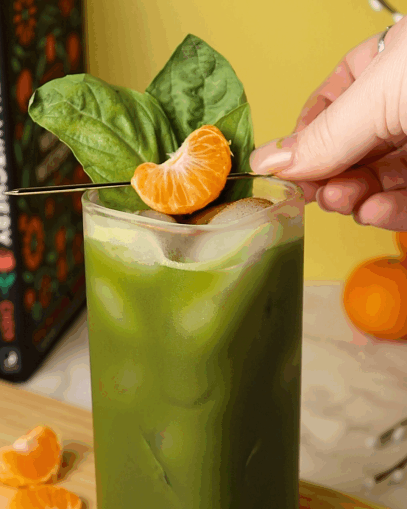 Basil and mandarin slice garnish atop a matcha soda in a rectangular glass.