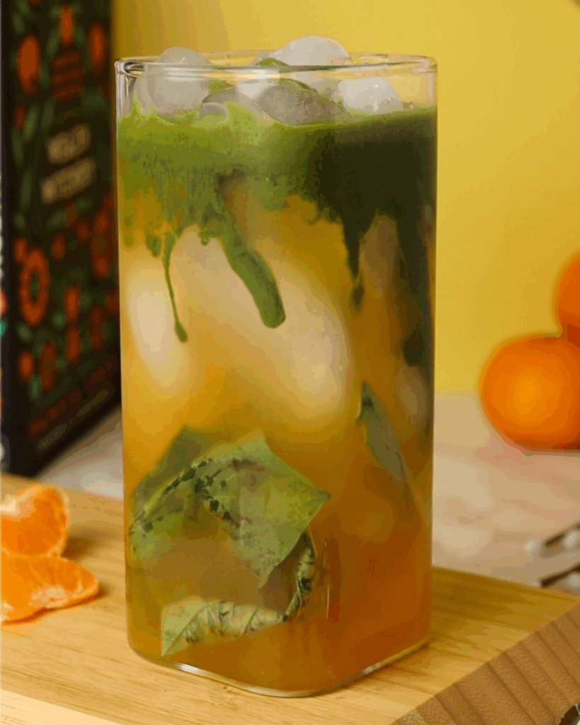Matcha layered atop mandarin orange juice in a square glass.