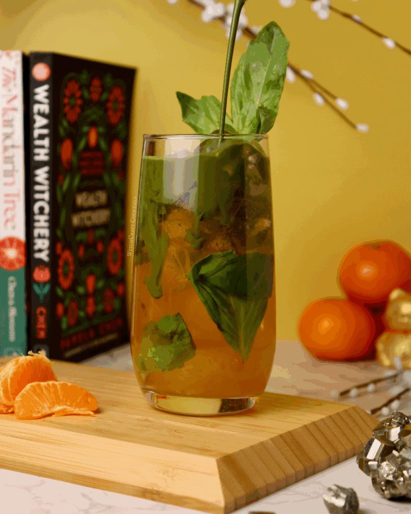 A citrus matcha mocktail in a cup, with orange on the bottom and green math pouring from above, garnished with a basil leaf.