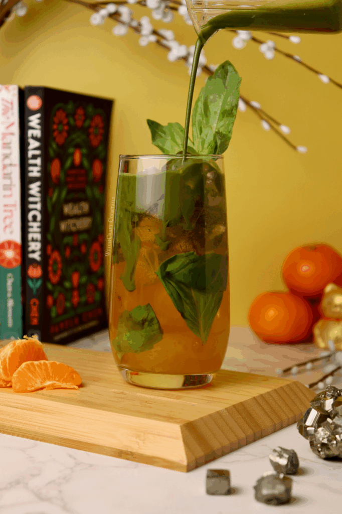 A matcha soda with orange mandarin juice on the bottom of the cup with green matcha pouring in from above.
