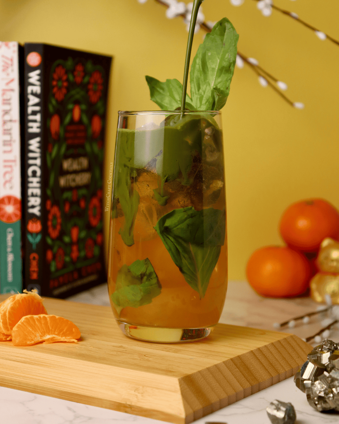 A citrus matcha mocktail in a cup, with orange on the bottom and green math pouring from above, garnished with a basil leaf.