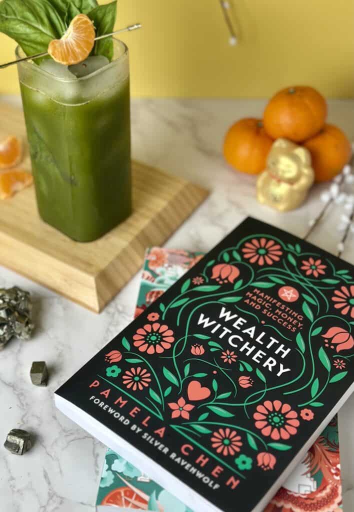 Wealth Witchy by Pamela Chen laying flat with a matcha soda in the top left corner.