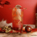 Red Aries cocktail in collins glass against a red background with gold accents.