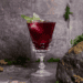 Red sangria with sage garnish in fancy glassware.
