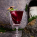 Red sangria with sage garnish in fancy glassware.
