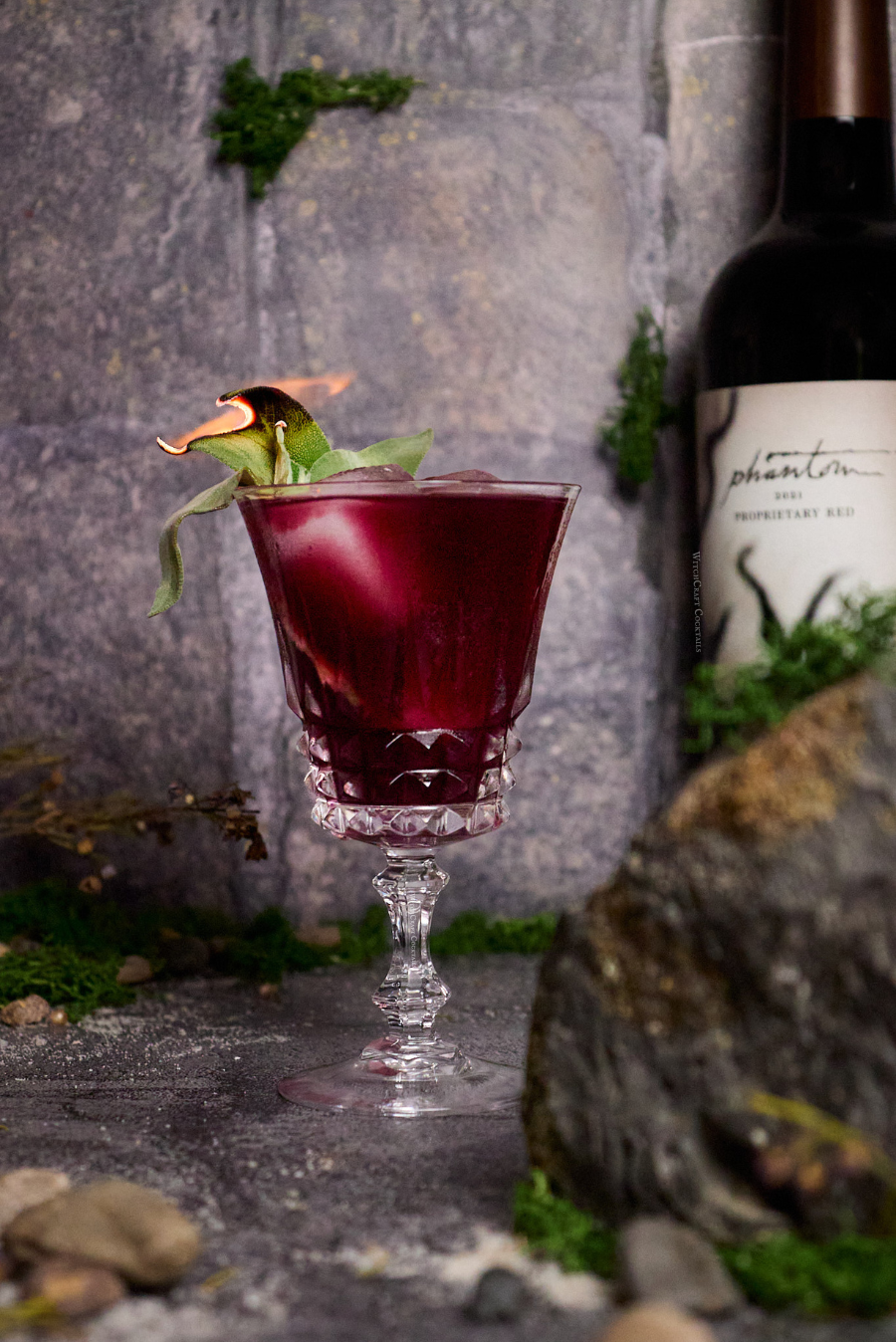 Red sangria with sage garnish in fancy glassware.