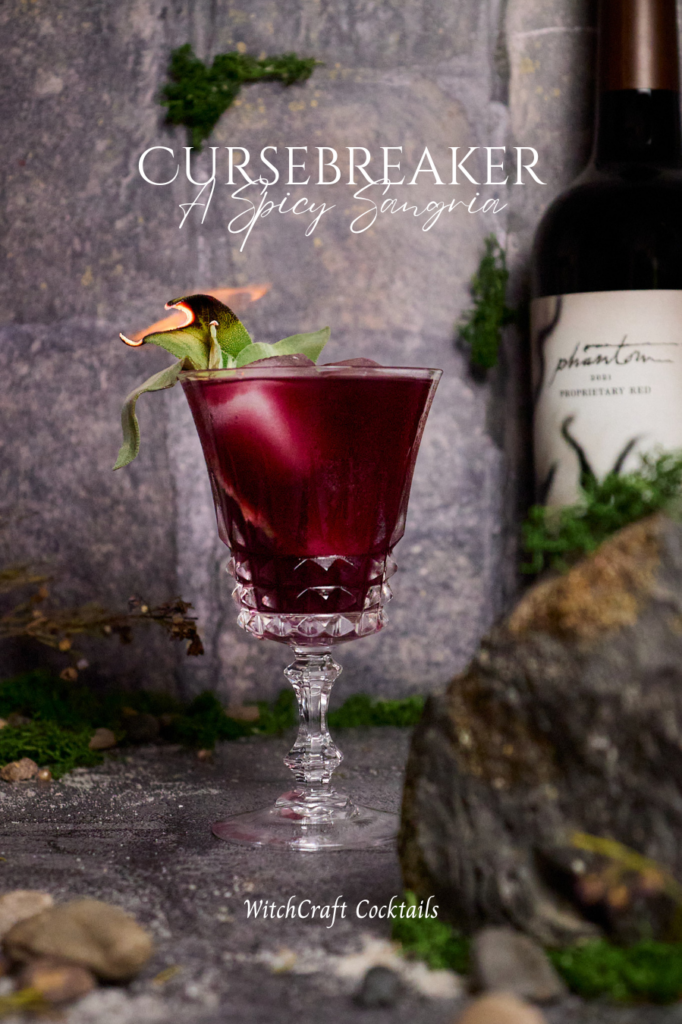Red sangria with sage garnish in fancy glassware, with the text: "Cursebreaker, A Spicy Sangria"