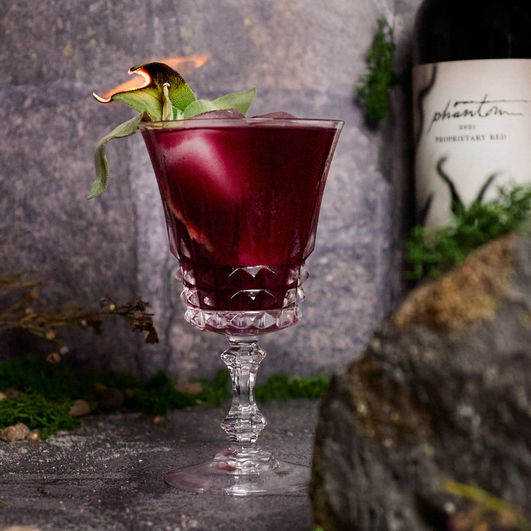 Red sangria with sage garnish in fancy glassware.